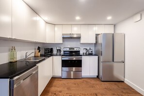 A modern kitchen with stainless steel appliances, white cabinetry, and a wooden floor. - Urban Haven | Modern Comfort in Downtown MTL (Montreal)