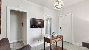Una sala moderna con un televisor de pantalla plana montado en la pared, una mesita de madera con una planta, y dos sofás grises.