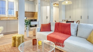 En moderne stue med sofa, sofabord i glas og et spiseområde med et bord dækket til to personer.