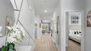 Ein moderner Hotelkorridor mit Holzboden, weißen Wänden und einem Essbereich mit Tisch und Orchideenpflanze.