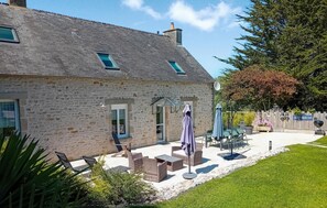 Une maison en pierre avec un patio, du mobilier d’extérieur et une enseigne indiquant « SAINT-HARCOUF ».