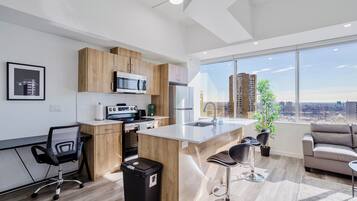 Une cuisine moderne avec des meubles en bois, un réfrigérateur en acier inoxydable et une grande fenêtre donnant sur un paysage urbain.