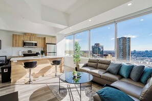 A modern apartment with a kitchen, a dining area, a living room with a sofa, and large windows offering a city view. - City Centre, Luxury Corner Suite, Near Rogers (Edmonton)