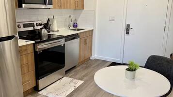 Une cuisine moderne avec des meubles en bois, des appareils électroménagers en acier inoxydable et une table de salle à manger ronde agrémentée d’une plante en pot.