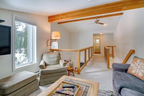 Ein großzügiges Wohnzimmer mit hohen Decken, einem Kamin, einem Fernseher und einer gemütlichen Sitzecke mit Sofa und Sesseln.