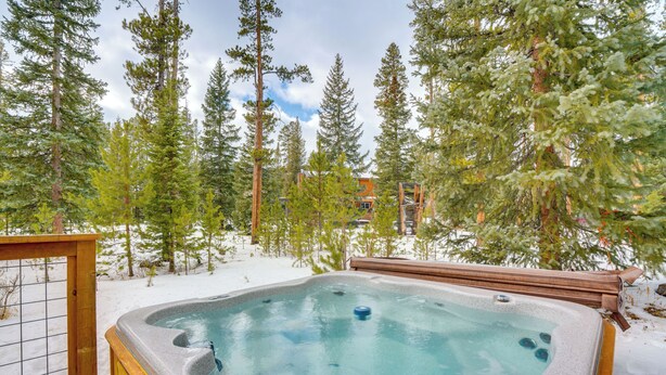 Un bain à remous entouré de neige et d’arbres, avec une terrasse en bois et une clôture en métal.