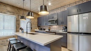 A modern kitchen with a central island, stainless steel appliances, and dark cabinetry. - Indoor Pool, Hot Tub! 'The Smoky Luxe Retreat' (Pigeon Forge)