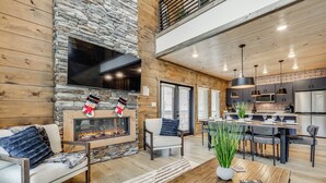 A modern living room with a stone fireplace, a dining area, and a kitchen with stainless steel appliances. - Indoor Pool, Hot Tub! 'The Smoky Luxe Retreat' (Pigeon Forge)
