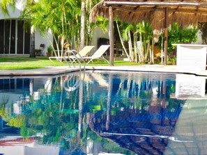 A swimming pool with clear blue water, surrounded by palm trees and lounge chairs.
