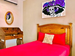 Ein Schlafzimmer mit einem hölzernen Bett, roter Bettwäsche, einem Nachttisch aus Holz und einem Spiegel mit Totenkopf-Design.