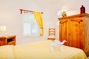 Un dormitorio con cama, un armario de madera, una silla, un escritorio con lámpara y una ventana con cortinas.