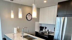 Eine moderne Küche mit Kochinsel, Edelstahlgeräten, Pendelleuchten und minimalistischem Design.