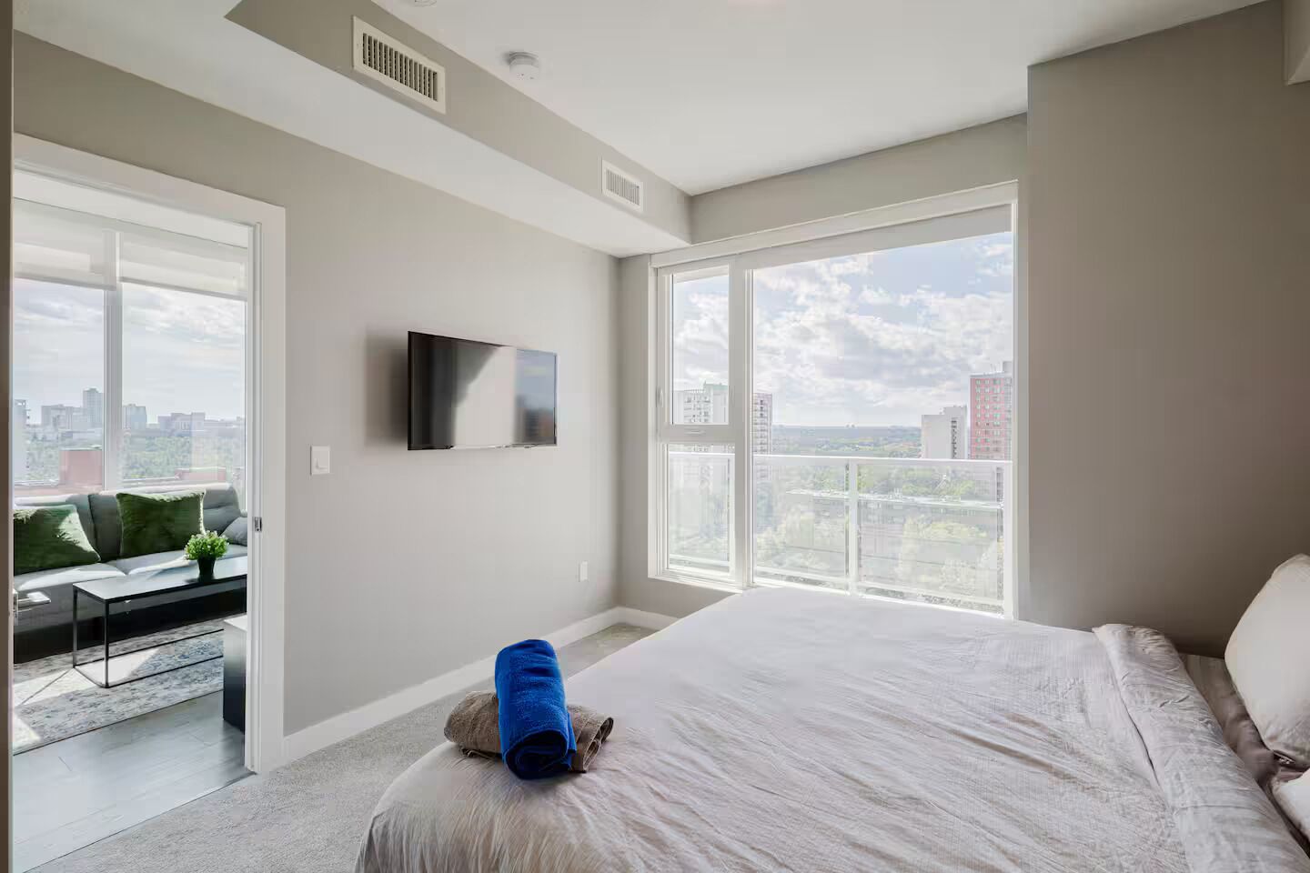 Ein modernes Schlafzimmer mit einem großen Bett, einem Wand-Fernseher und Blick auf die Stadt durch große Fenster.