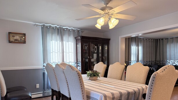 Ein Esszimmer mit einem Tisch, gedeckt für sechs Personen, umgeben von sechs Stühlen. Über dem Tisch befindet sich ein Deckenventilator mit Beleuchtung.