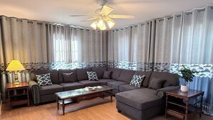 Ein Wohnzimmer mit Ecksofa, Couchtisch, Beistelltisch und Deckenventilator.