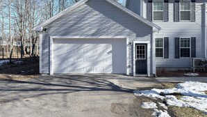Ein zweistöckiges Haus mit Garage, kleiner Veranda und Auffahrt.