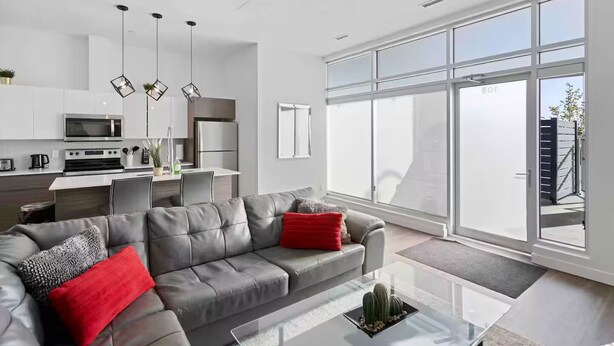 A modern living room with a grey leather sofa, a glass coffee table, and a large window offering a view of the city. - Luxury 2BR, 10ft ceiling, 5 mins from Dt (Edmonton)
