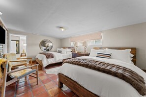 Een hotelkamer met twee bedden, een houten stoel, een ronde spiegel en een raam met uitzicht.
