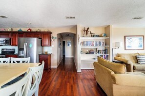 A spacious living area with a kitchen, a bookshelf, and a seating area. - Easy Gulf-View Retreat w/ Big Deck, Outdoor Shower & Pet Friendly (Bolivar Peninsula)