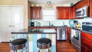 A kitchen with wooden cabinets, a stainless steel refrigerator, a microwave, a stove, and two bar stools. - Easy Gulf-View Retreat w/ Big Deck, Outdoor Shower & Pet Friendly (Bolivar Peninsula)