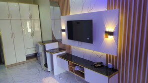 A modern hotel room with a flat-screen TV mounted on the wall, a desk with a telephone, and a small shelf. - 517VIP Suites and Apartments Awka (Awka)