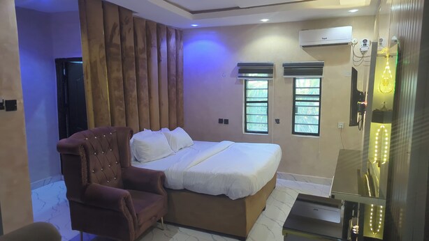 A bedroom with a bed, a chair, a window, and an air conditioning unit. - 517VIP Suites and Apartments Awka (Awka)