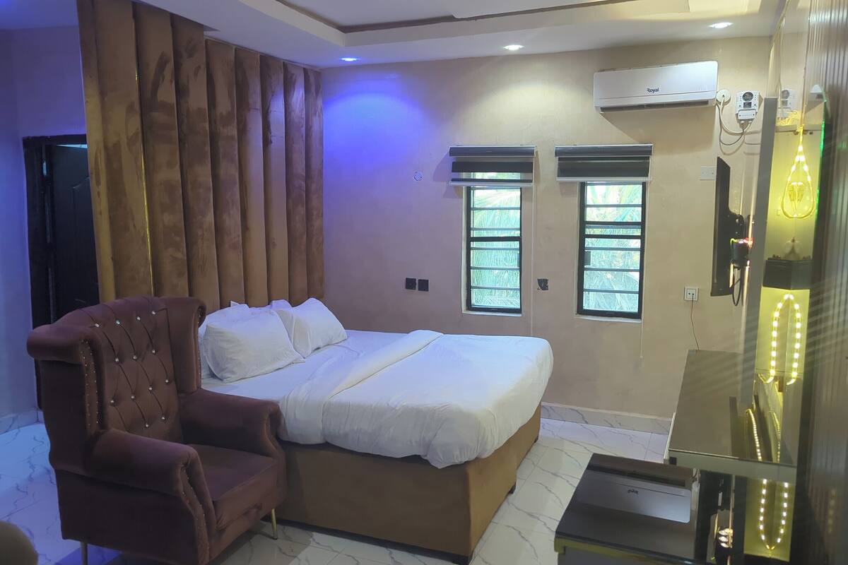 Un dormitorio con cama, una silla, un ventanal y un equipo de aire acondicionado.