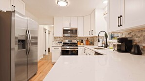 Una cocina moderna con electrodomésticos de acero inoxidable, armarios blancos y una encimera de mármol.