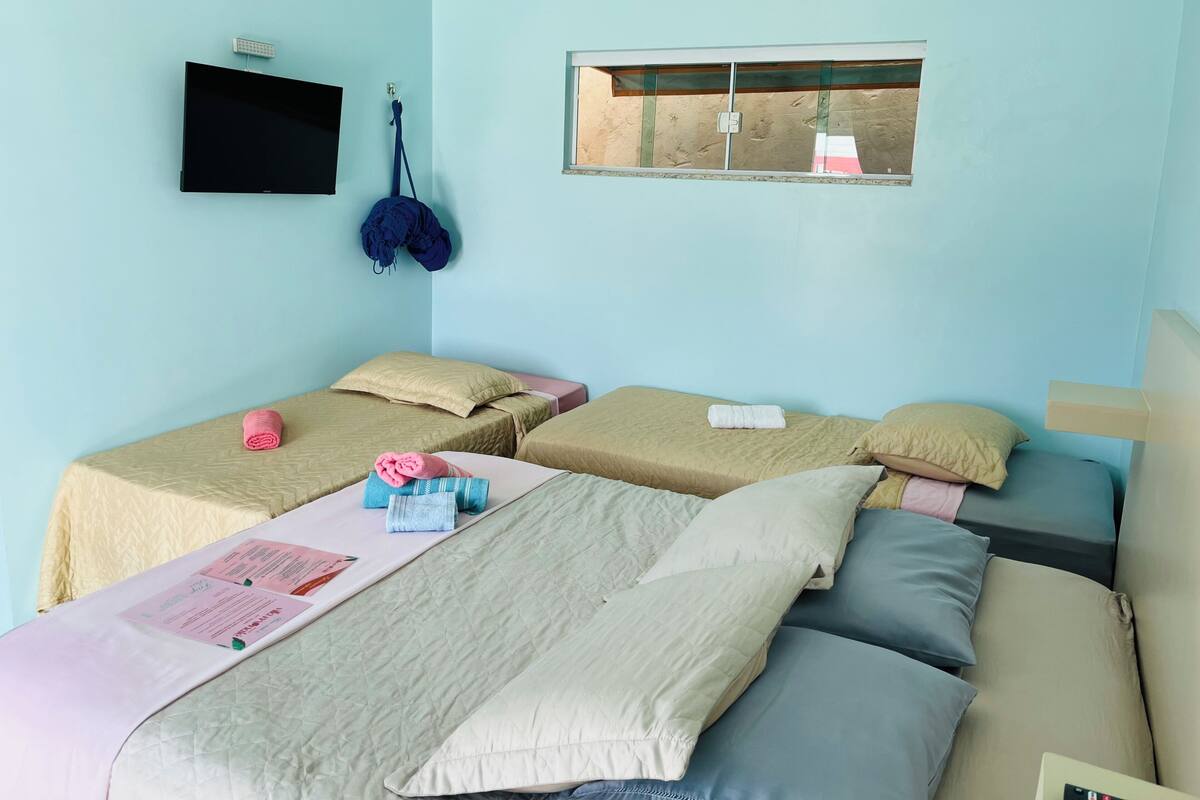Una habitación con dos camas, una ventana, un televisor y aire acondicionado instalado en la pared.