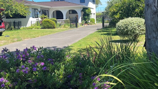 Een huis met twee verdiepingen, een voortuin, een oprit en een keurig onderhouden tuin met paarse bloemen.