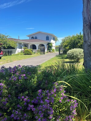 Ein zweistöckiges Haus mit Veranda, Auffahrt und einem gepflegten Garten mit violetten Blumen.