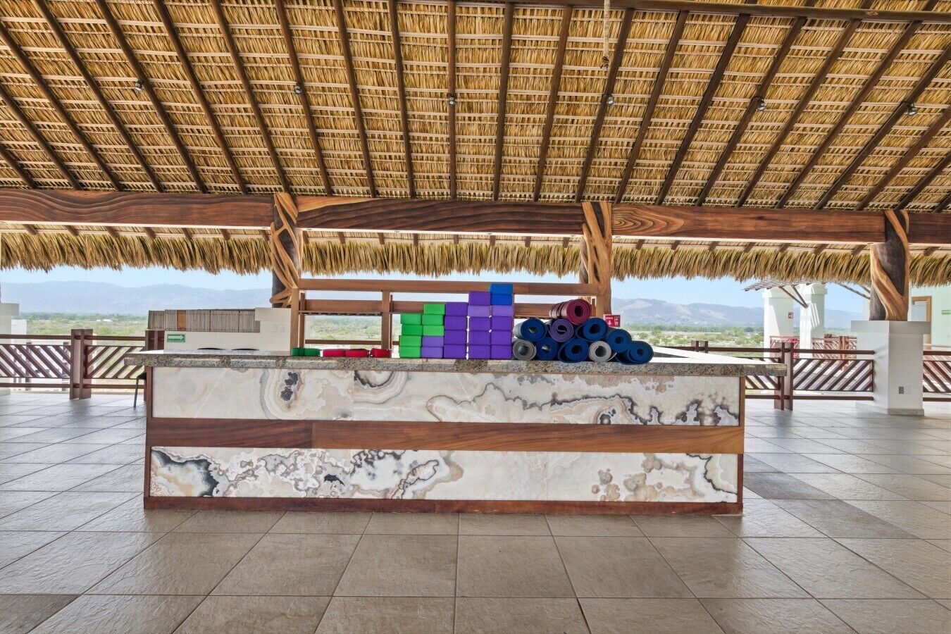 Una terraza al aire libre con techo de paja, una barra de mármol y bloques de colores al fondo.