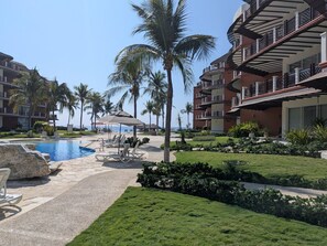 A resort pool area with lounge chairs, palm trees, and a clear view of the ocean. - https://169666_1.holidayfuture.com/ (Bajos de Chila)