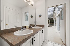 Ein Badezimmer mit zwei Waschbecken, einem großen Spiegel und Blick auf die Außenpatio-Terrasse.