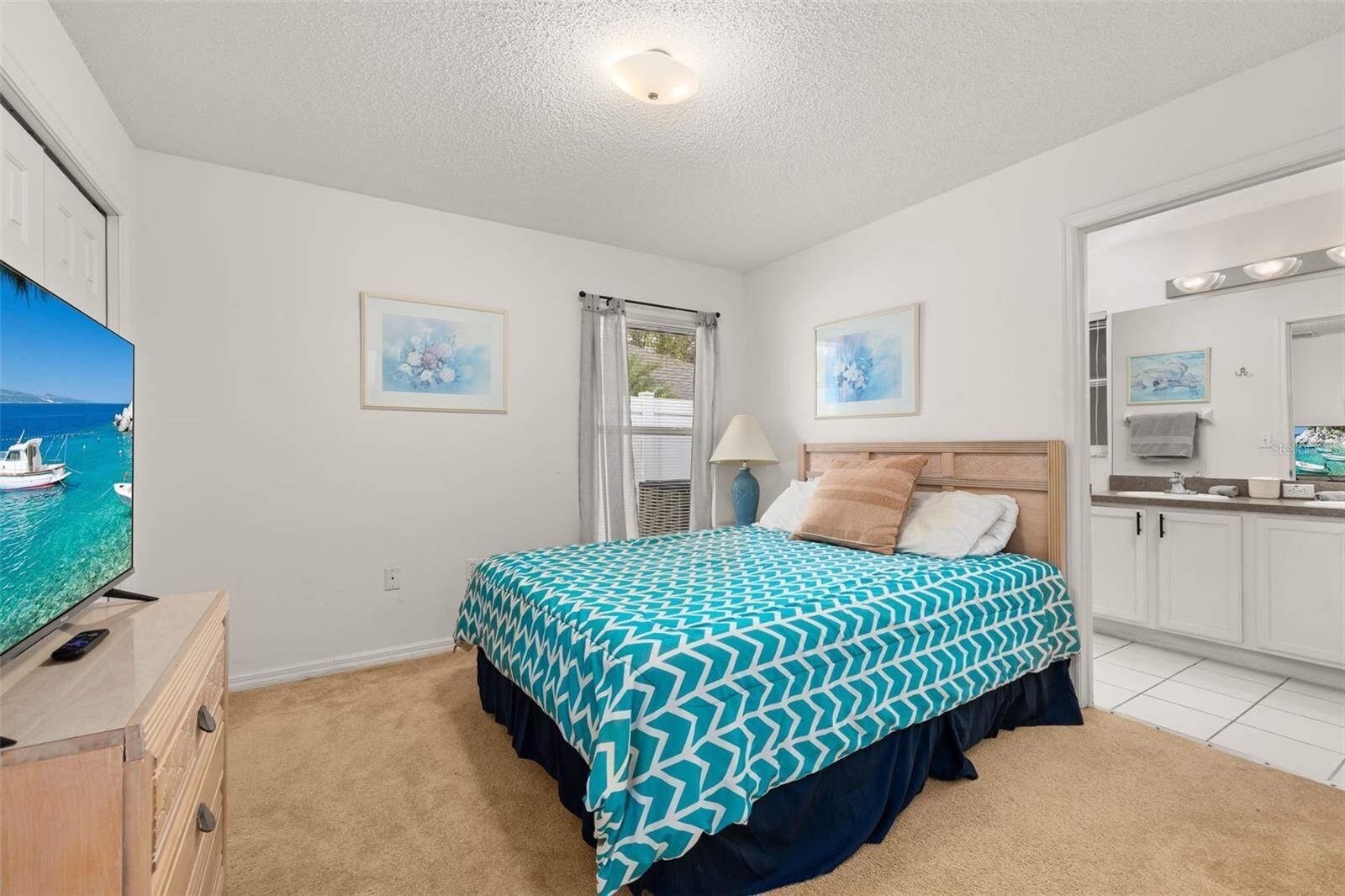 A bedroom with a bed, a TV, a dresser, and a bathroom with a mirror.