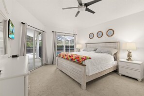 Ein Schlafzimmer mit Bett, Nachttisch, Deckenventilator und einer Schiebetür zu einem Balkon.