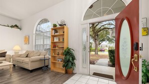 A modern living room with a wooden bookshelf, a sofa, and a dining table. - Cozy 4 Bedroom Home with South Facing Pool & 4 bedroom home (Davenport)