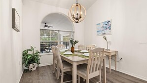 A dining area with a wooden table, chairs, a chandelier, and a view through a window. - Cozy 4 Bedroom Home with South Facing Pool & 4 bedroom home (Davenport)