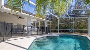 A swimming pool with a clear blue water, surrounded by a white deck and a covered patio area with chairs and a ceiling fan. - Cozy 4 Bedroom Home with South Facing Pool & 4 bedroom home (Davenport)