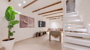 Ein modernes Wohnzimmer mit einer großen Topfpflanze, einer Couch, einem Fernseher und einer Treppe.
