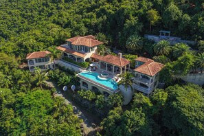Une grande maison à plusieurs étages, dotée d’une piscine et entourée d’une végétation luxuriante.