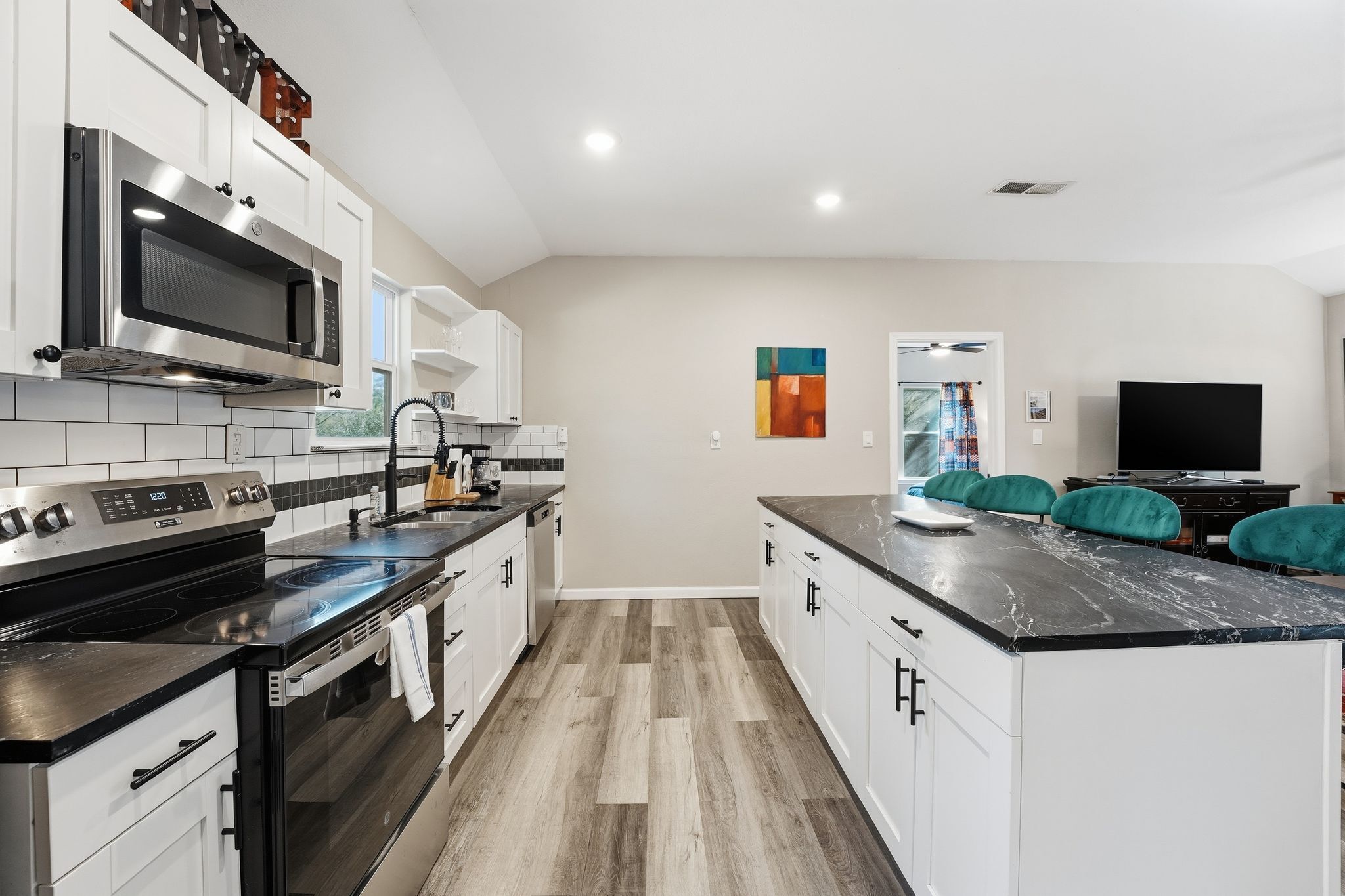 Una cocina moderna con electrodomésticos de acero inoxidable, una encimera negra y sillas color turquesa.