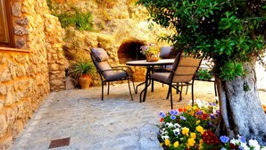 An outdoor patio with stone walls, a brick floor, and a round table with chairs. There is a potted plant and a flower arrangement on the table. - Almoguer Rural Complex (Frailes)