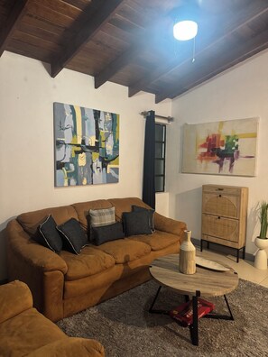 A living room with a brown sofa, two abstract paintings, a wooden cabinet, and a small table with a vase. - Cozy 2-bedroom house in tranquil West Terrace with AC (West Terrace)