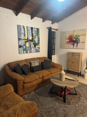 A living room with a brown sofa, two abstract paintings, a wooden cabinet, and a round coffee table. - Cozy 2-bedroom house in tranquil West Terrace with AC (West Terrace)