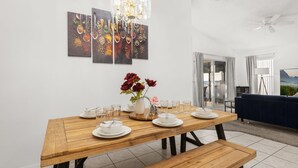 Een eetruimte met een houten tafel gedekt voor vier personen, een vaas met rode bloemen en een moderne kroonluchter.