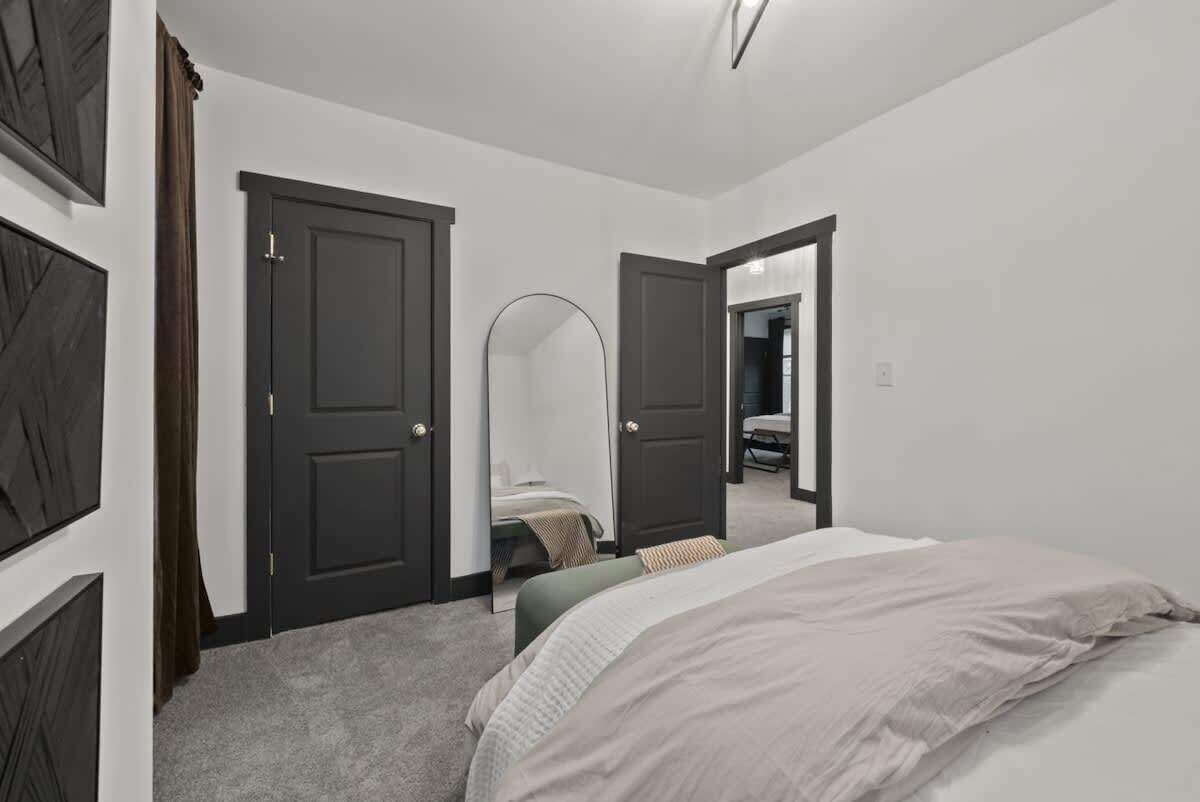 Une chambre à coucher avec un lit, une chaise et un miroir. Il y a deux portes, dont l’une mène à une salle de bain.