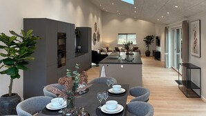Eine moderne Küche mit dunklen Schränken, einer zentralen Kochinsel und einem Essbereich mit Tisch für vier Personen.