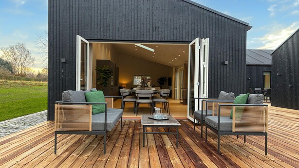 Eine moderne Außenpatio mit Essbereich, Holzterrasse und einer großen offenen Tür zu einem Innenraum.