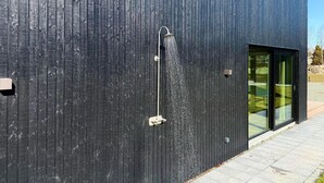 Un edificio moderno con paneles exteriores de madera vertical, una estructura metálica en la pared y puerta de entrada de vidrio.